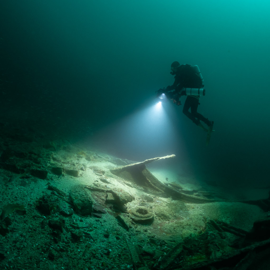 Rebreather diver with photogrammetry rig lighting sandy wreck debris below, Saint-Malo, Brittany, France