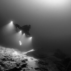 Black and white diver beaming four lights over rocky wreck rubble, Saint-Malo, Brittany, France