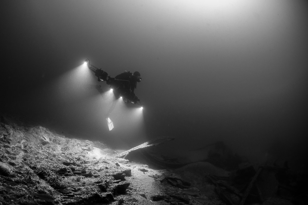 Black and white diver beaming four lights over rocky wreck rubble, Saint-Malo, Brittany, France