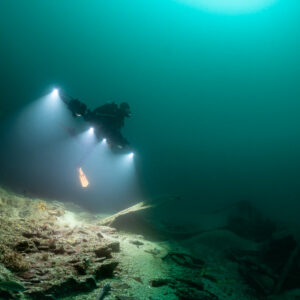 Rebreather diver hovering above wreck rubble with light beams in green water, Saint-Malo, Brittany, France