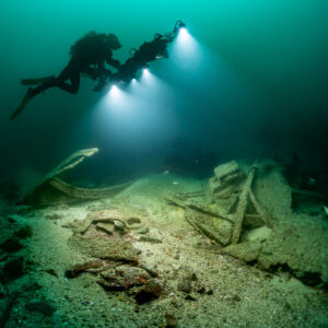 Diver gliding over collapsed wreck frames with photogrammetry lights on, Saint-Malo, Brittany, France