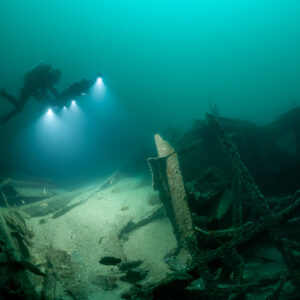 Diver lighting wreck debris with upright steel frames in foreground, Saint-Malo, Brittany, France