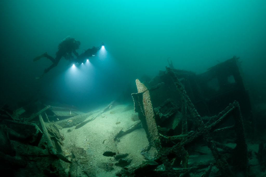 Diver lighting wreck debris with upright steel frames in foreground, Saint-Malo, Brittany, France
