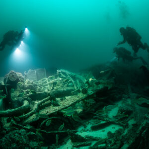 Three divers over wreck machinery and pipes with a shoal of fish, Saint-Malo, Brittany, France