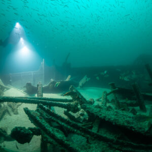 Diver lighting wreck pipework under a dense shoal of small fish, Saint-Malo, Brittany, France