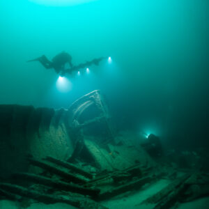 Two divers with lights exploring collapsed wreck frames, vertical framing, Saint-Malo, Brittany, France