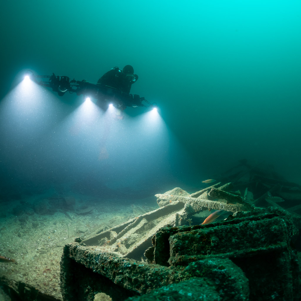 Rebreather diver flying four lights above a wreck winch structure, Saint-Malo, Brittany, France