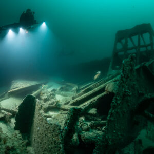 Rebreather diver beside a tall wreck frame lighting the debris field, Saint-Malo, Brittany, France