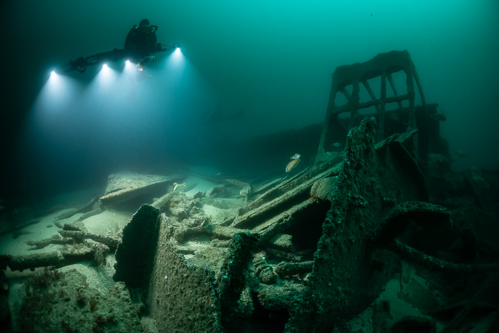 Rebreather diver beside a tall wreck frame lighting the debris field, Saint-Malo, Brittany, France