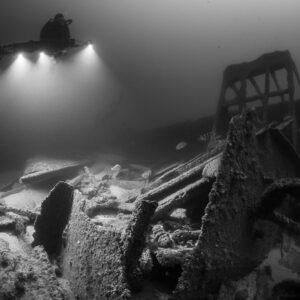Black and white diver with four lights beside a tall wreck frame, Saint-Malo, Brittany, France