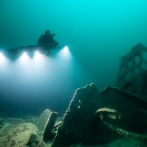 Diver lighting the seabed beside a tall lattice wreck structure, Saint-Malo, Brittany, France