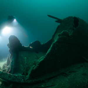 Diver lighting a torn wreck bow section rising from the sand, Saint-Malo, Brittany, France