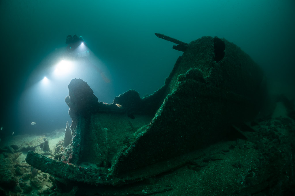 Diver lighting a torn wreck bow section rising from the sand, Saint-Malo, Brittany, France