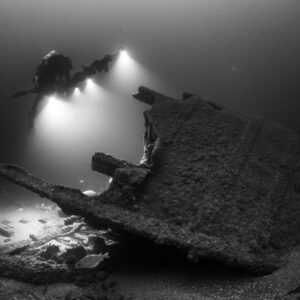 Black and white diver lighting fish beside a tilted wreck section, Saint-Malo, Brittany, France