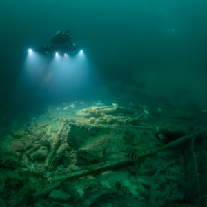 Diver lighting a debris-strewn wreck floor from above, landscape view, Saint-Malo, Brittany, France