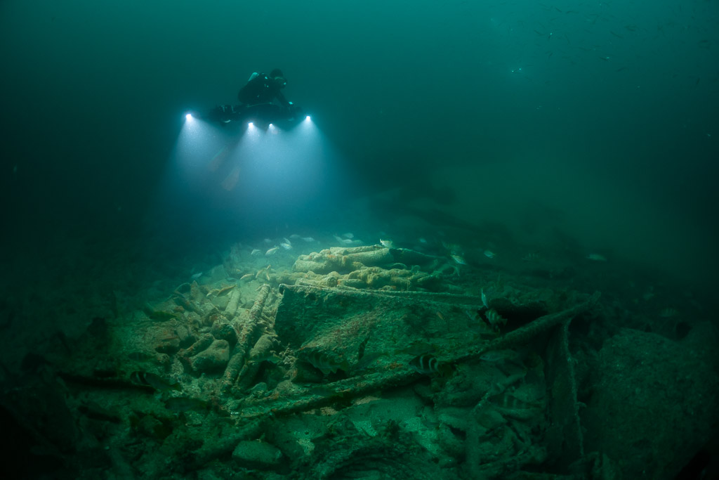 Diver lighting a debris-strewn wreck floor from above, landscape view, Saint-Malo, Brittany, France