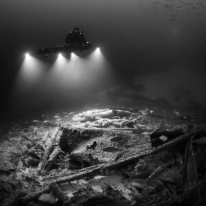 Black and white diver lighting the wreck floor with fish below, Saint-Malo, Brittany, France