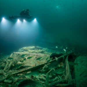 Diver directly above lit wreck debris with fish swimming through, Saint-Malo, Brittany, France