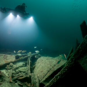 Diver lighting wreck plates and fish behind an angled steel frame, Saint-Malo, Brittany, France