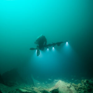 Distant diver with four lights above wreck debris, narrow vertical framing, Saint-Malo, Brittany, France