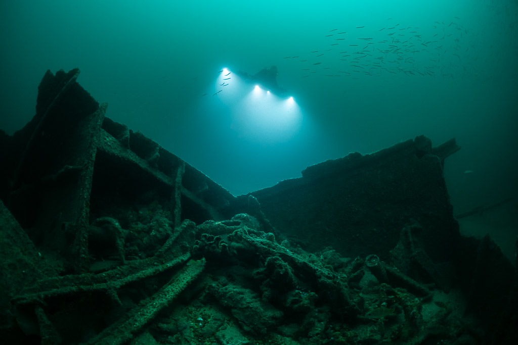 Distant diver lights framed between two broken wreck hull sides, Saint-Malo, Brittany, France