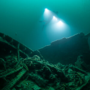 Diver lights closer between two broken hull sides over tangled debris, Saint-Malo, Brittany, France