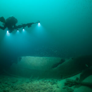 Diver with photogrammetry rig over smooth curved hull plates on sand, Saint-Malo, Brittany, France