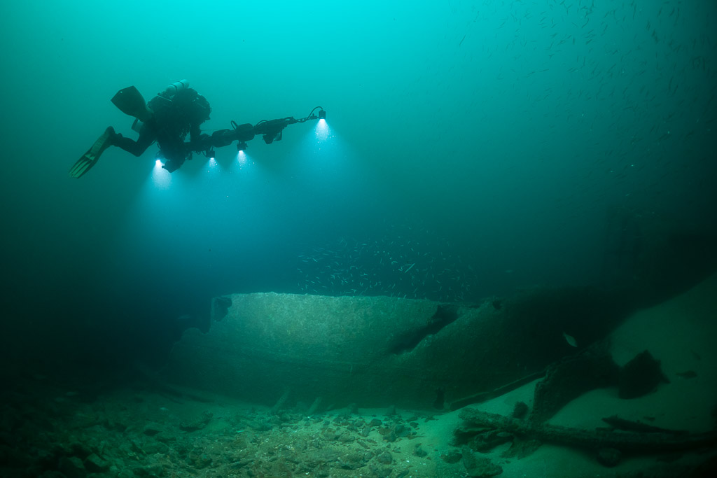 Diver with photogrammetry rig over smooth curved hull plates on sand, Saint-Malo, Brittany, France