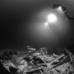 Black and white diver shining a bright light down on fish over debris, Saint-Malo, Brittany, France
