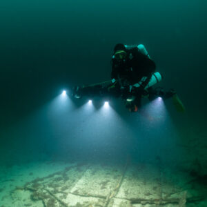 Rebreather diver facing camera with rig lighting flat wreck plates, Saint-Malo, Brittany, France