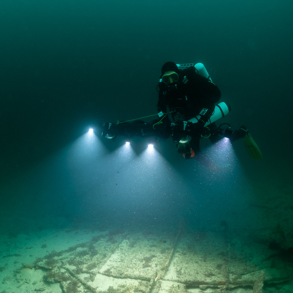 Rebreather diver facing camera with rig lighting flat wreck plates, Saint-Malo, Brittany, France