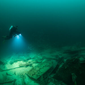 Small distant diver lighting a wide wreck debris field, Saint-Malo, Brittany, France
