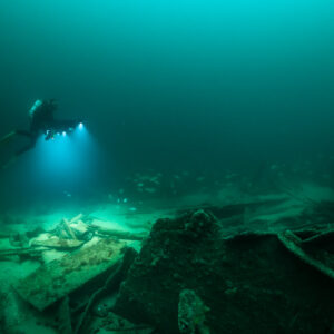 Distant diver lighting wreck debris beside an upright hull frame, Saint-Malo, Brittany, France