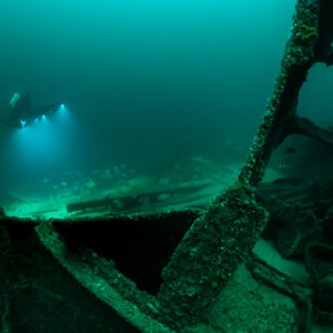 Diver lights in distance beyond an encrusted wreck frame in foreground, Saint-Malo, Brittany, France
