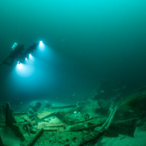 Diver with rig crossing a low wreck debris field in green water, Saint-Malo, Brittany, France