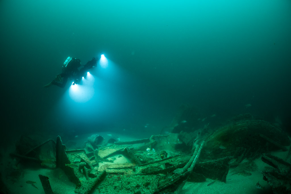 Diver with rig crossing a low wreck debris field in green water, Saint-Malo, Brittany, France