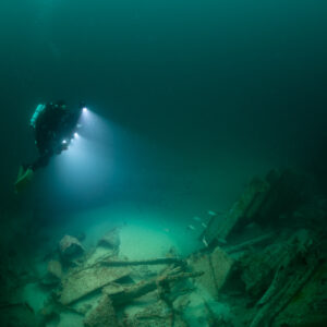 Diver descending with lights toward wreck debris, tight framing, Saint-Malo, Brittany, France