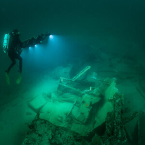 Rebreather diver upright with rig beside lit wreck machinery, Saint-Malo, Brittany, France