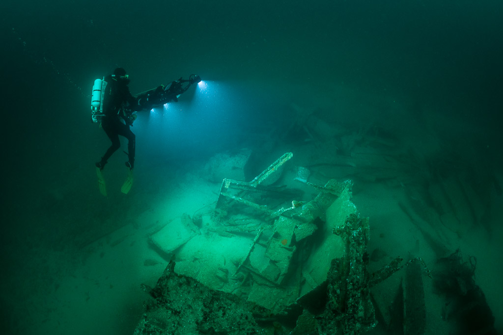 Rebreather diver upright with rig beside lit wreck machinery, Saint-Malo, Brittany, France