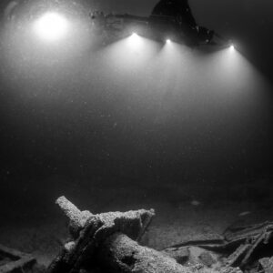 Black and white diver lighting a cylindrical wreck fitting, vertical, Saint-Malo, Brittany, France
