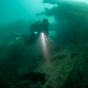 Rebreather diver with torch beside the encrusted hull of the Laplace, Laplace wreck, Brittany, France