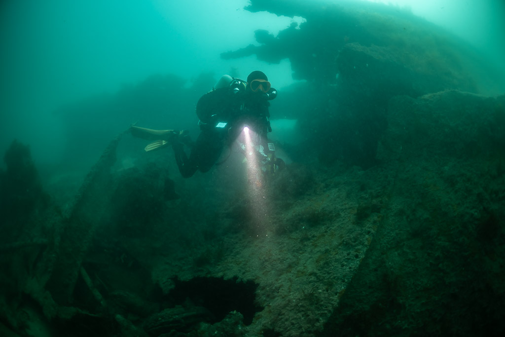 Rebreather diver with torch beside the encrusted hull of the Laplace, Laplace wreck, Brittany, France