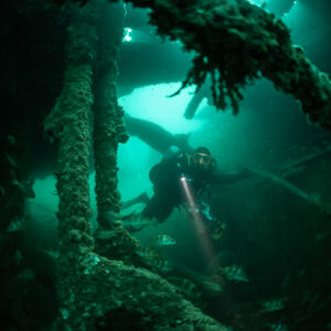 Diver with torch framed by encrusted pillars inside the Laplace wreck, Laplace wreck, Brittany, France