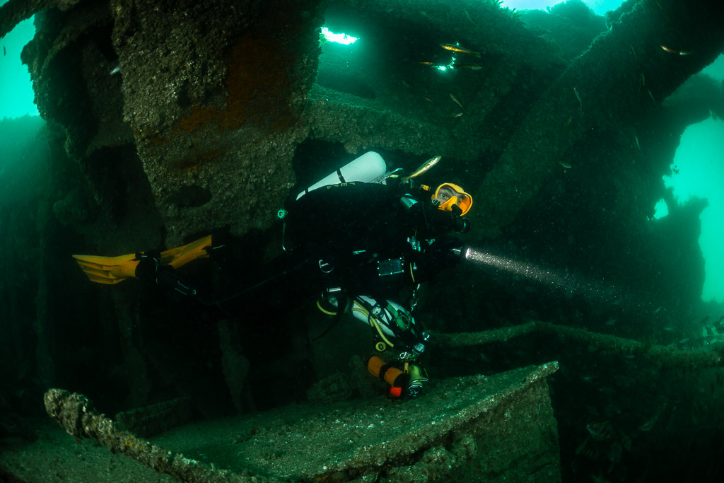 Rebreather diver with torch and yellow fins inside the Laplace wreck, Laplace wreck, Brittany, France