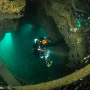 Diver framed in a rusty wreck archway with pouting below, Laplace wreck, Brittany, France