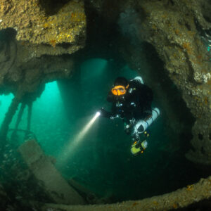 Diver aiming torch down inside a rusty wreck arch with pouting, Laplace wreck, Brittany, France