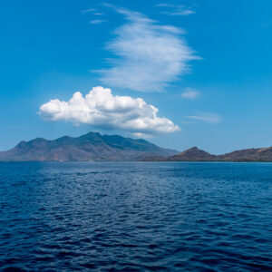 Volcanic island under white clouds seen across the open sea, West Flores, Banda Sea, Indonesia