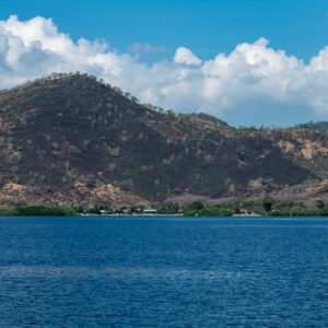 Dry green hills over a calm bay under cumulus clouds, Shark Point, Banda Sea, Indonesia