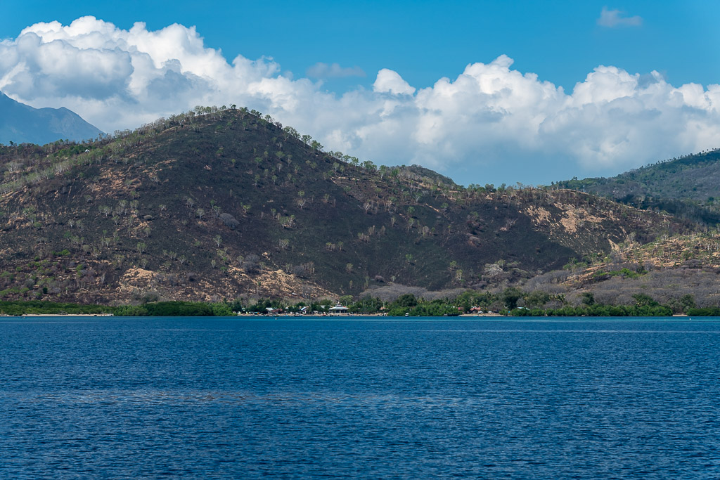Collines sèches et vertes au-dessus d’une baie calme sous des cumulus, Shark Point, mer de Banda, Indonésie