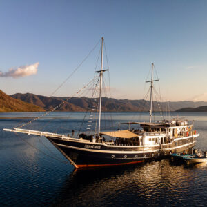 Phinisi liveaboard with tender anchored in a calm bay at golden hour, Bacatan Wall, Banda Sea, Indonesia